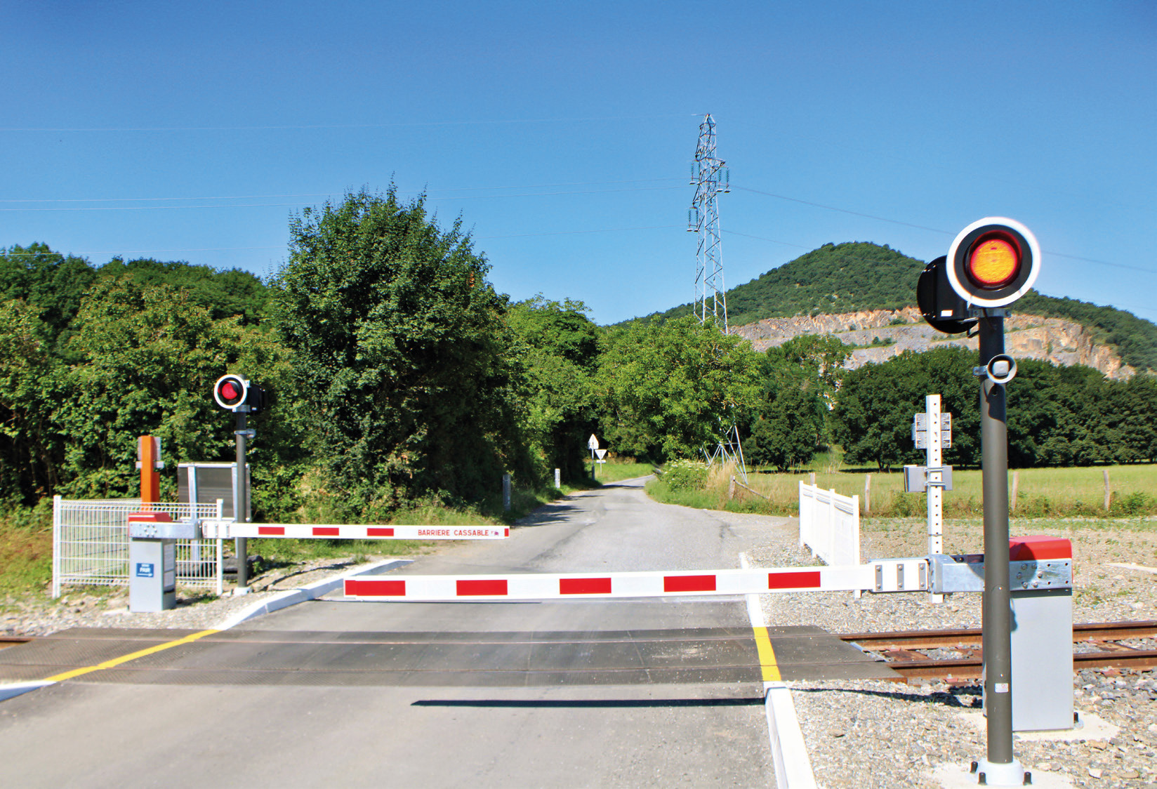 Le PN Flex en position fermée avec clignotement des signaux lumineux, ici le PN n° 2 de Montréjeau - Luchon. Le haut-parleur situé sur le mât diffuse le fichier son reproduisant la sonnerie des PN SNCF (19 juin 2025)